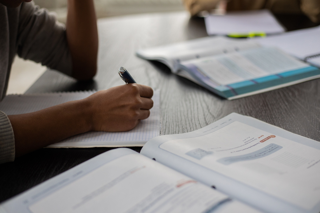 Crop black person writing in workbook while studying